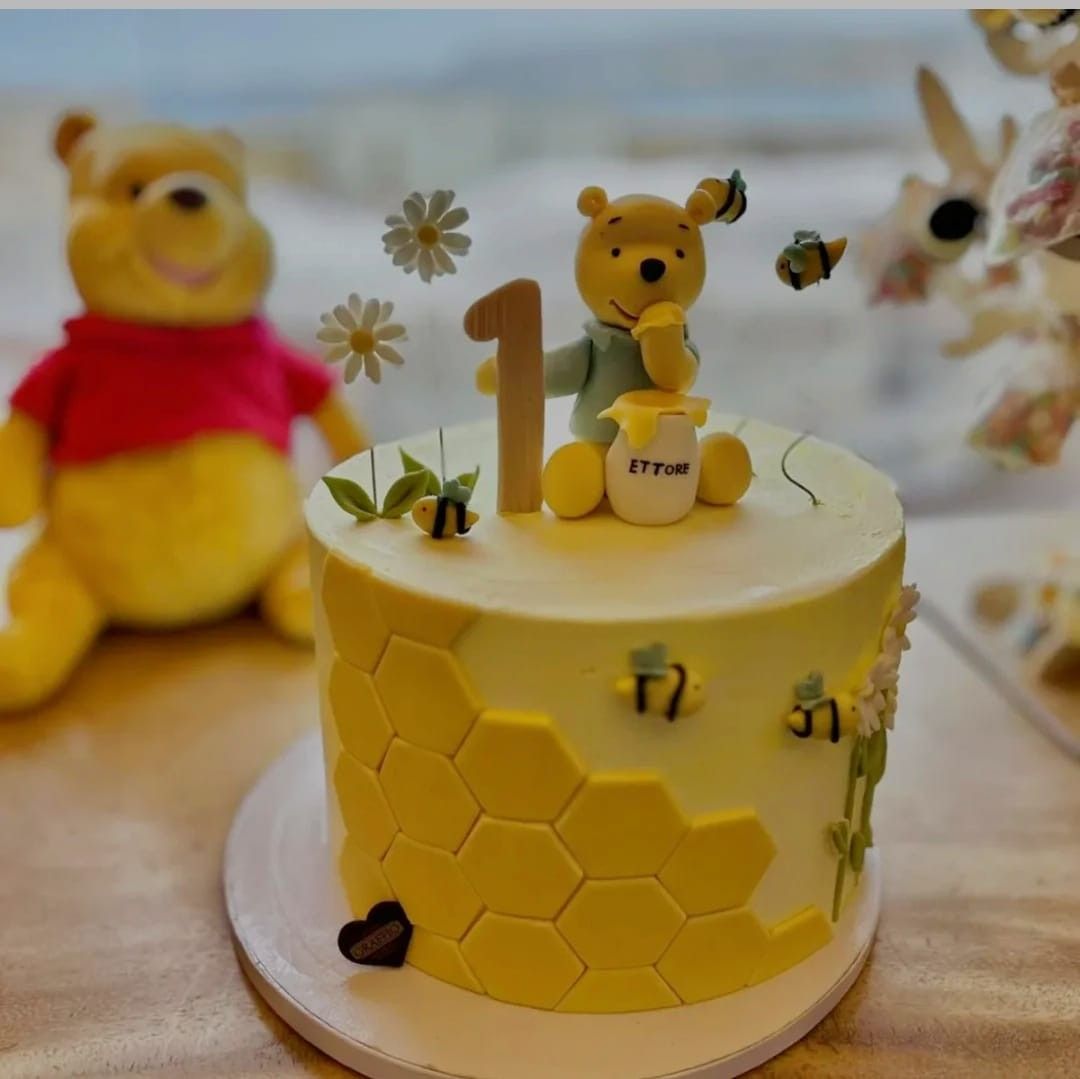 Torta a tema Winnie the Pooh per il primo compleanno. Glassa gialla, motivo a nido d'ape, orsetto Winnie the Pooh, api, margherite.