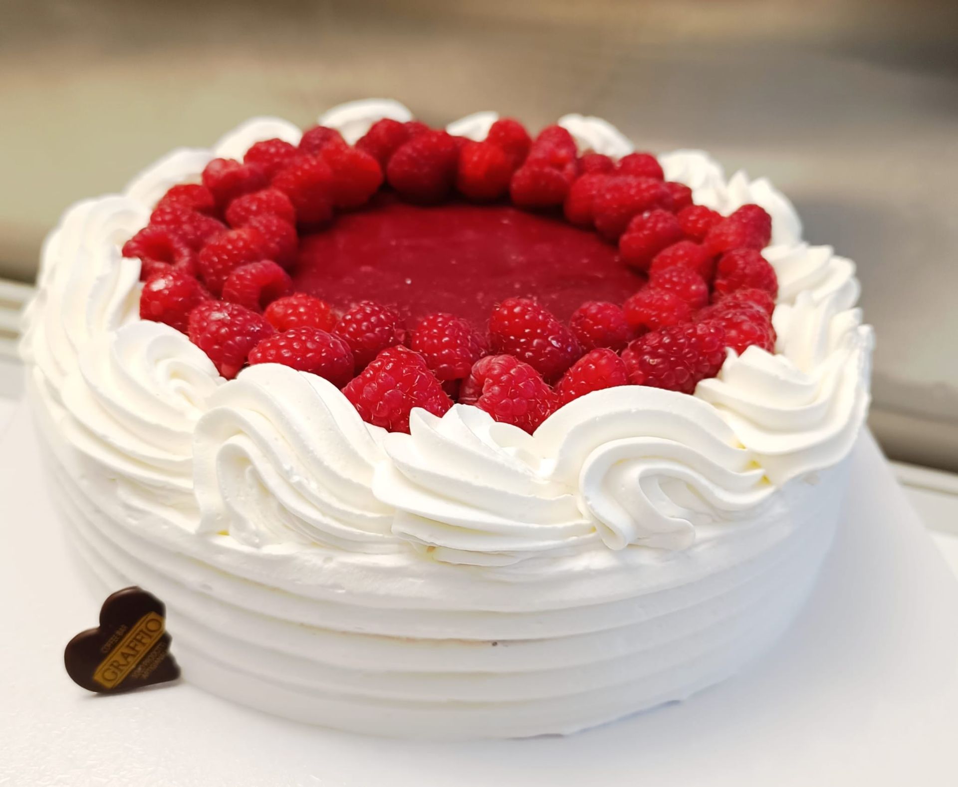 Torta bianca con glassa montata, ripieno di lamponi e lamponi freschi.