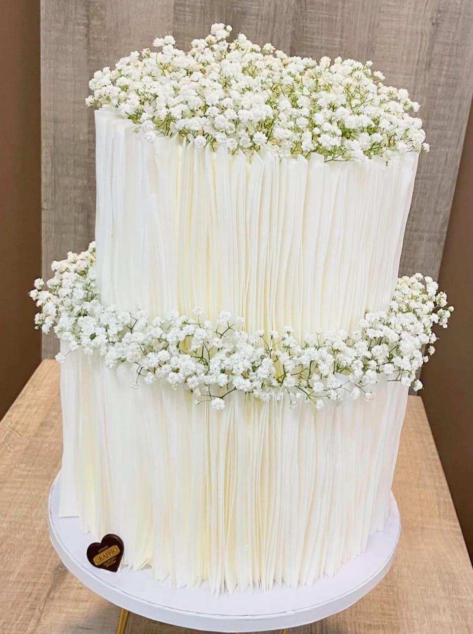 Torta bianca a due piani, con struttura verticale, con un anello e una parte superiore ricoperta di fiori bianchi di gypsophila.