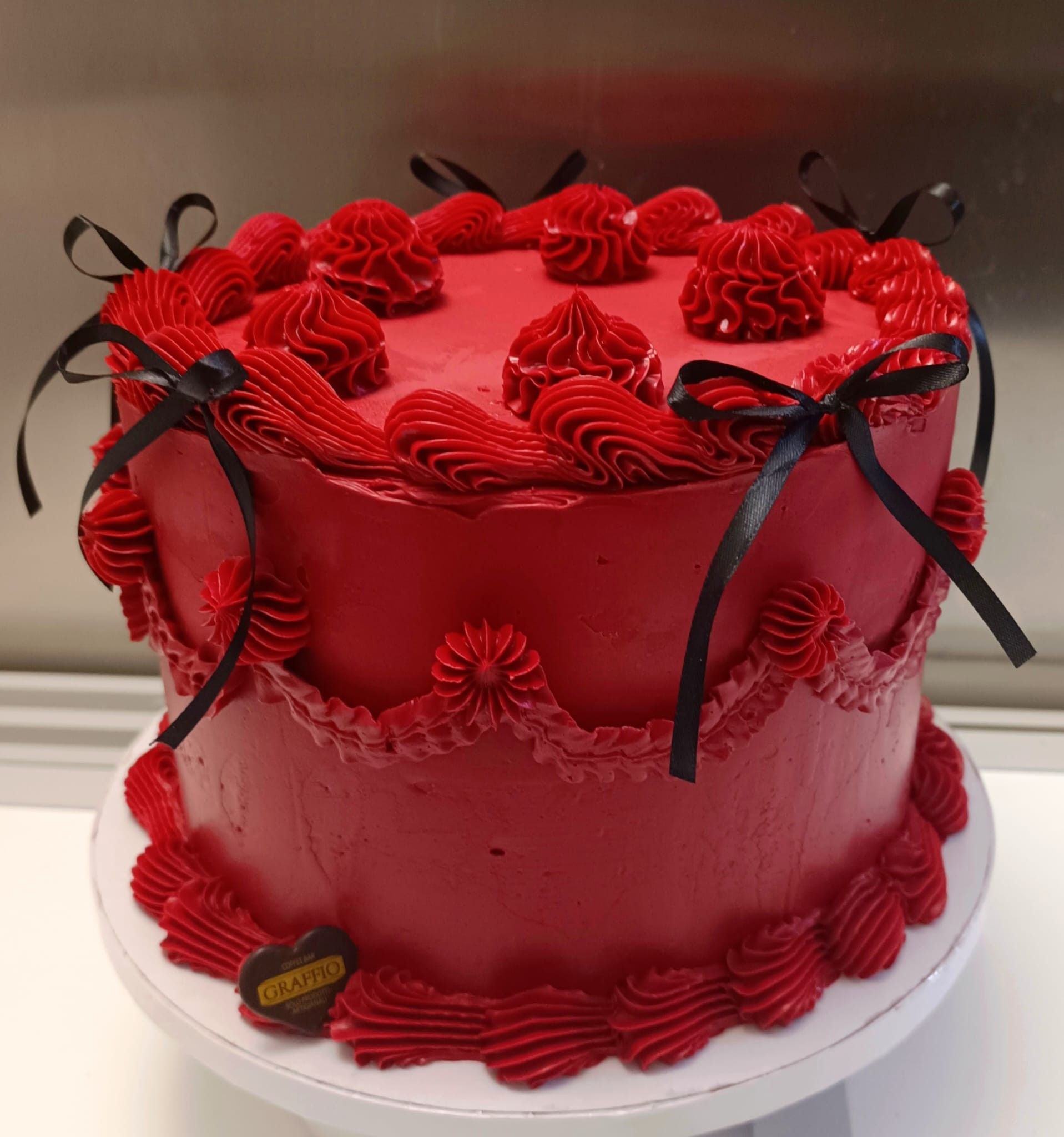 Torta glassata rossa con fiocchi di nastro nero.