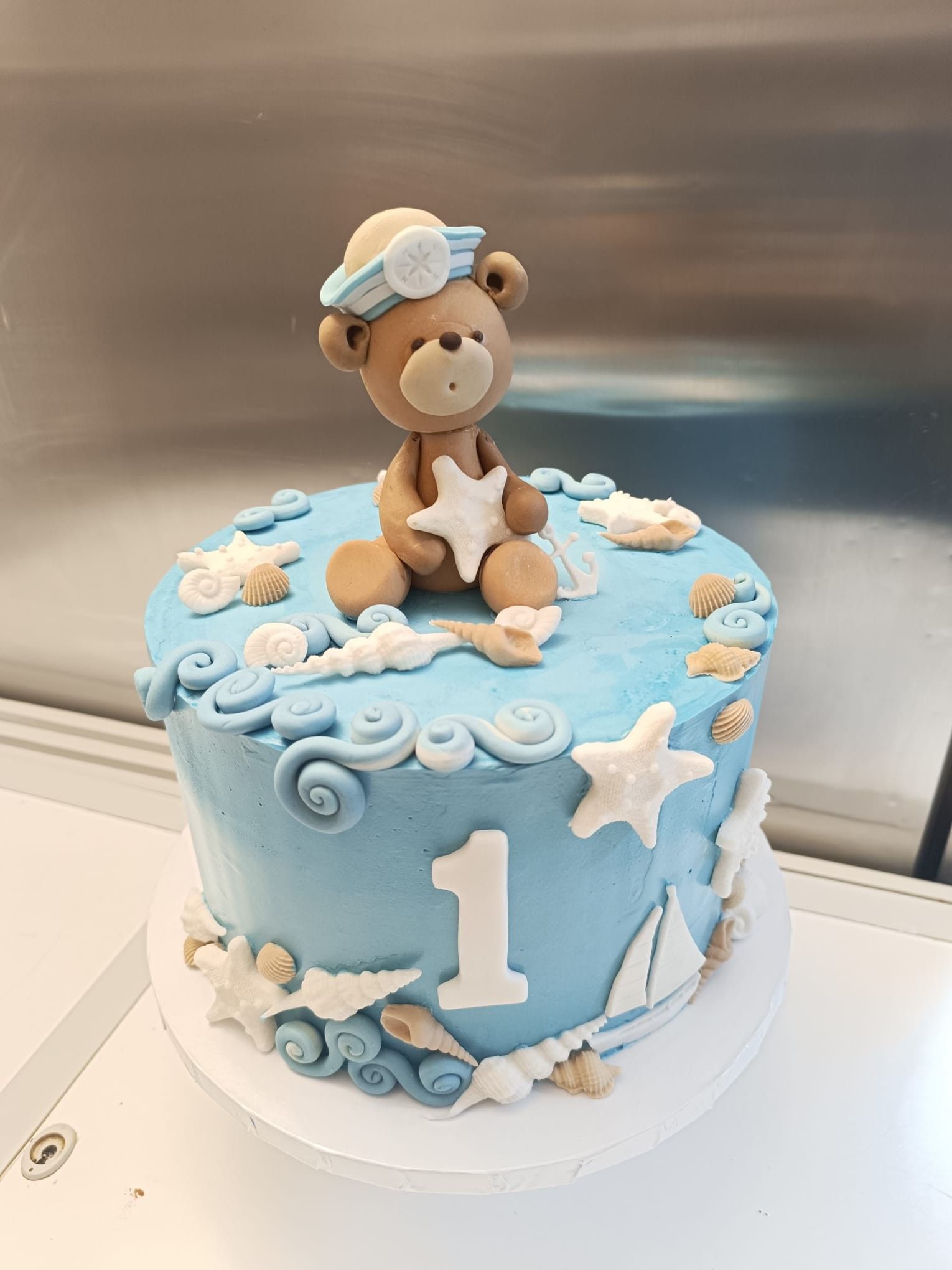 Torta glassata blu decorata con un tema nautico, un orsacchiotto e il numero uno.