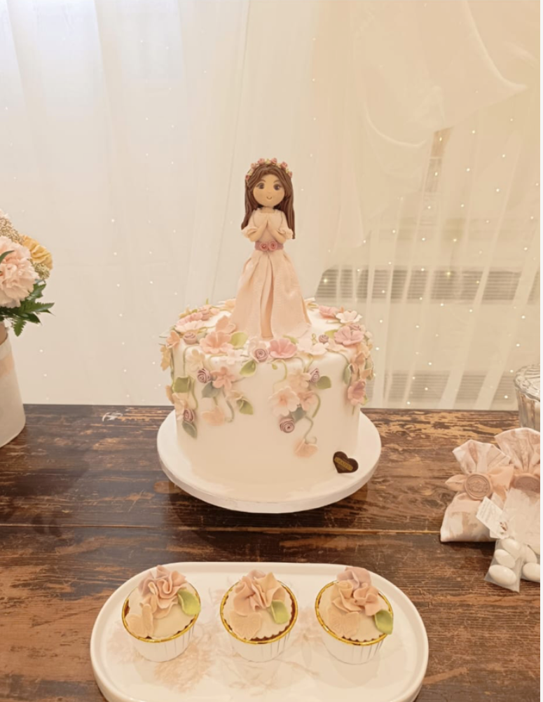 Torta con bambola in cima e cupcakes su un tavolo di legno, decorato con fiori rosa.