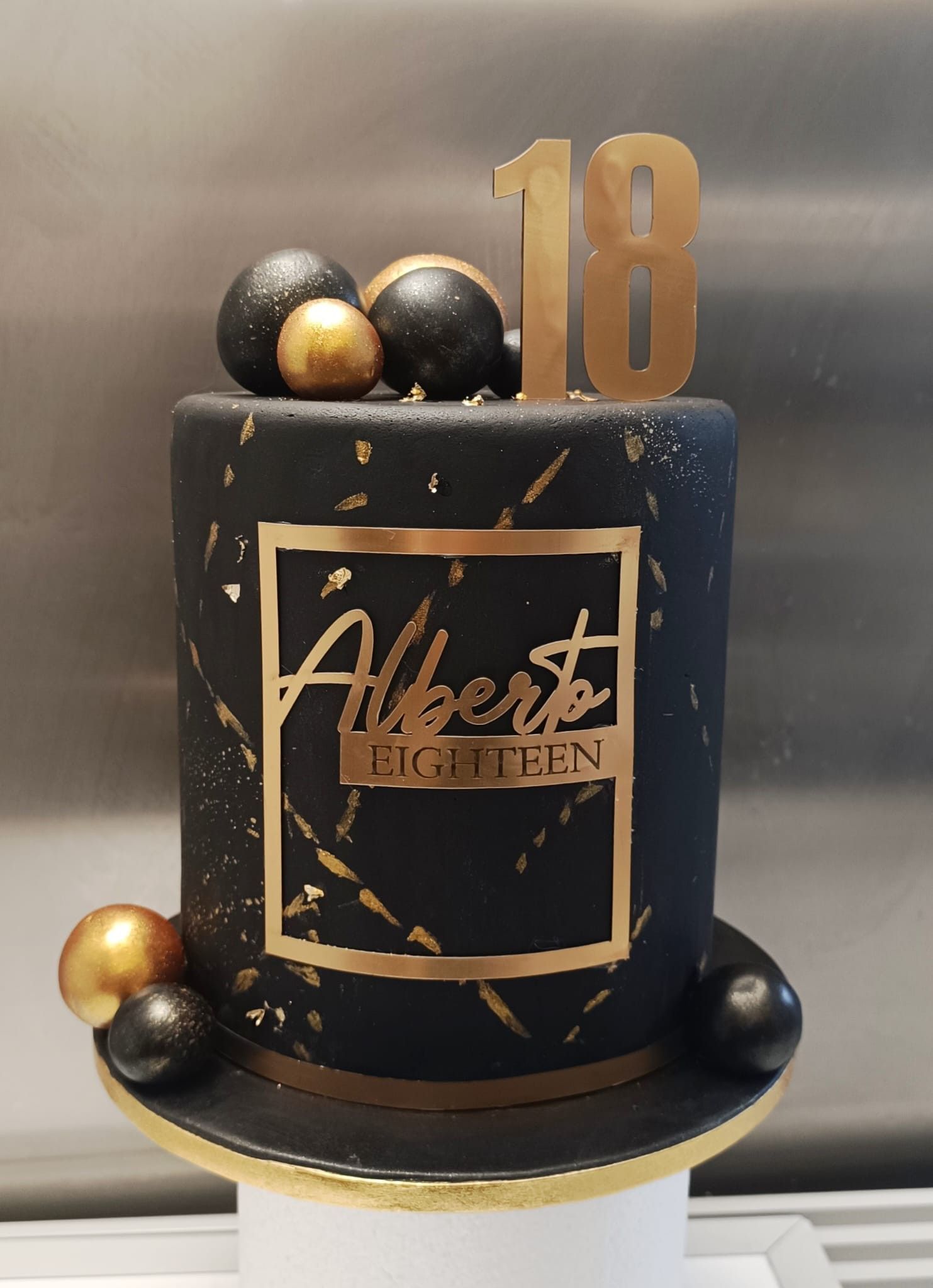 Torta di compleanno nera con dettagli dorati, targhetta con il nome 