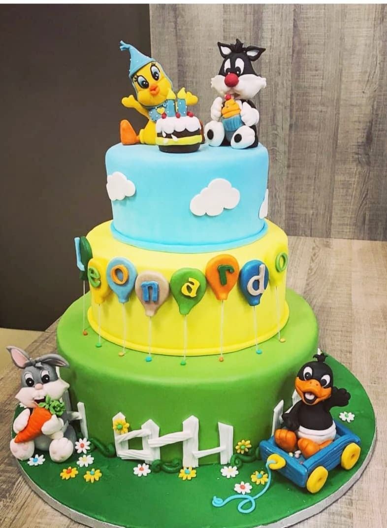 Torta a tre piani raffigurante i personaggi dei cartoni animati: Titti, Silvestro, Bugs Bunny e Daffy Duck su strati blu, giallo e verde.