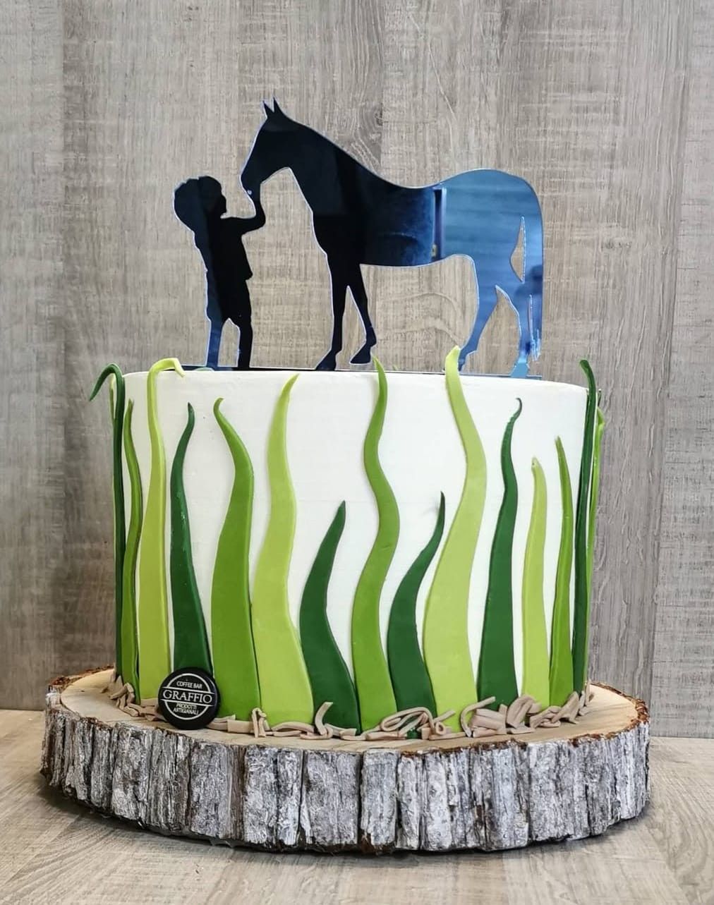 Torta decorata con la sagoma di un ragazzo e di un cavallo, crema al burro color verde erba, su una base di legno.