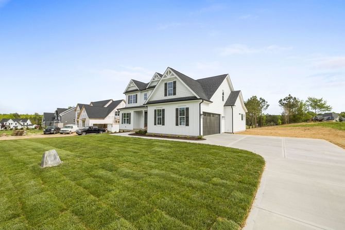 Large white suburban house with a curved driveway and green lawn under a clear blue sky