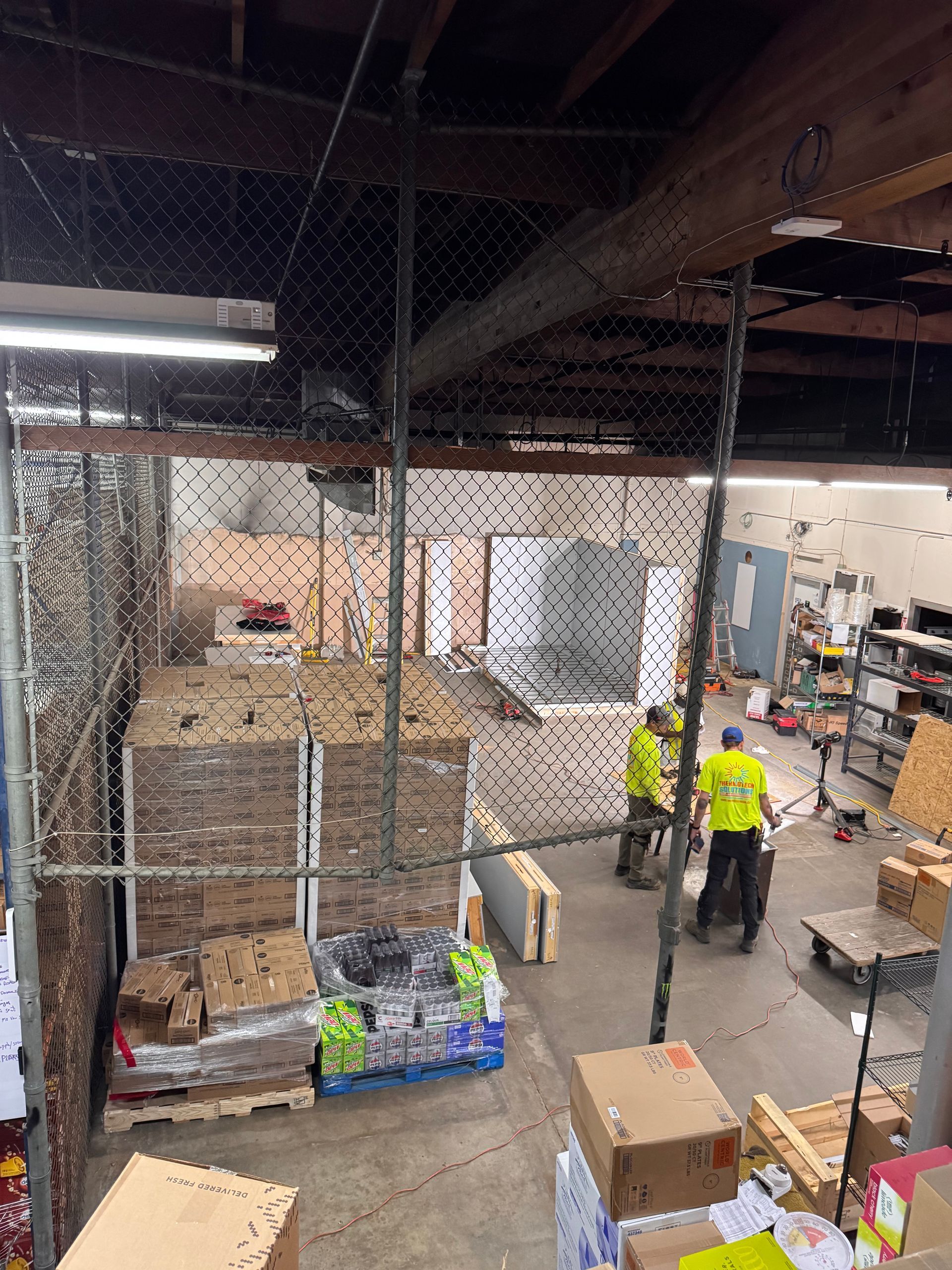 Warehouse interior: Workers in safety vests near boxes, pallets, and metal fencing.
