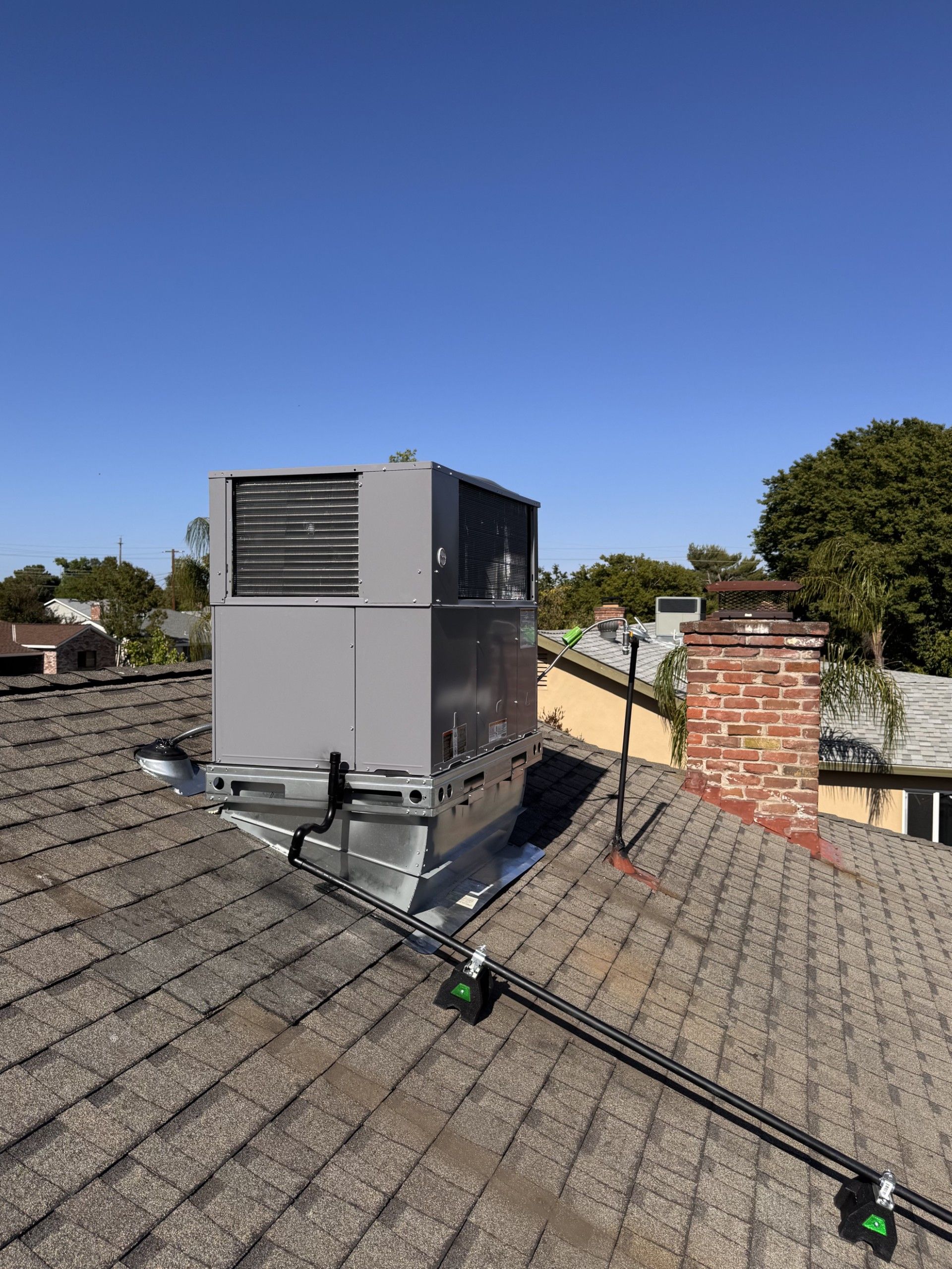 White air conditioning unit mounted on a dark gray wooden exterior wall with white conduit pipes.