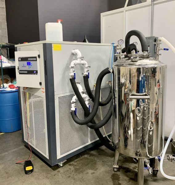 Industrial chilling machine with connected stainless steel tank in a workshop setting.