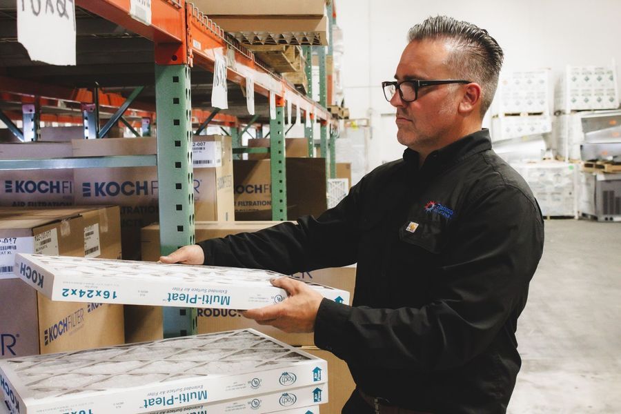 Man in glasses holding filter boxes in a warehouse.