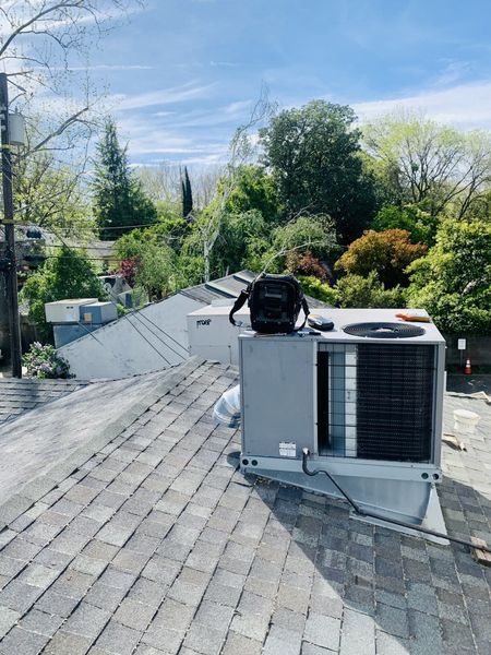 HVAC unit on a rooftop with a toolbox. Cloudy sky and surrounding trees.