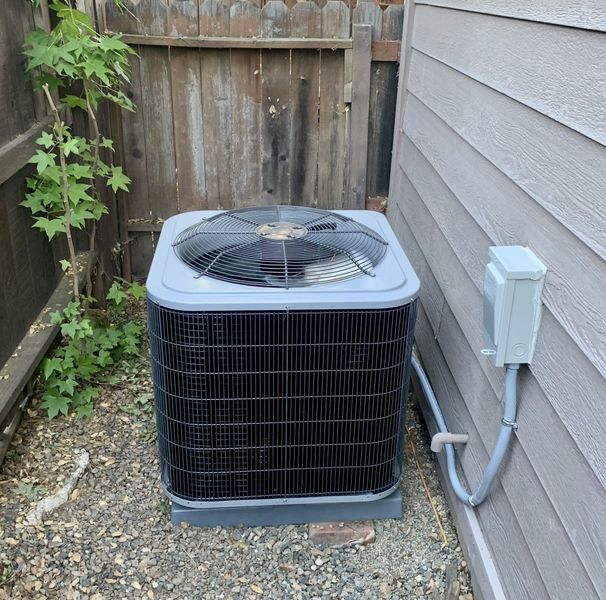Air conditioning unit next to a wooden fence and gray siding.
