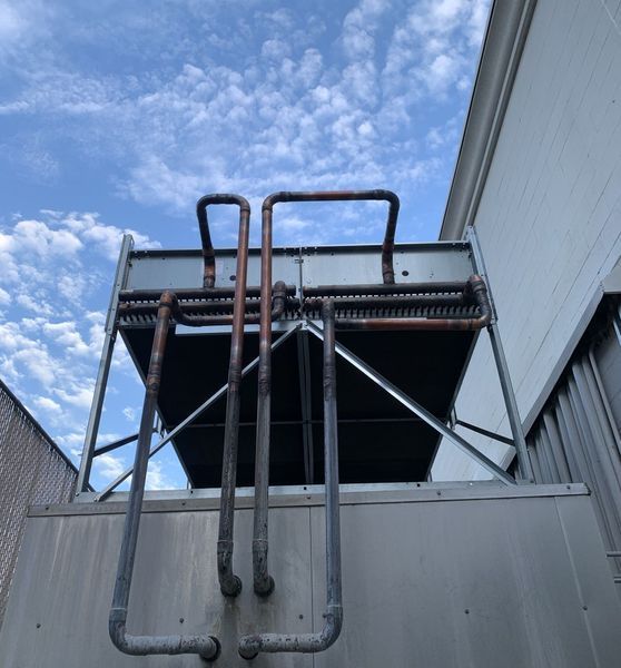 Cooling unit on a building roof with copper pipes against a cloudy sky.