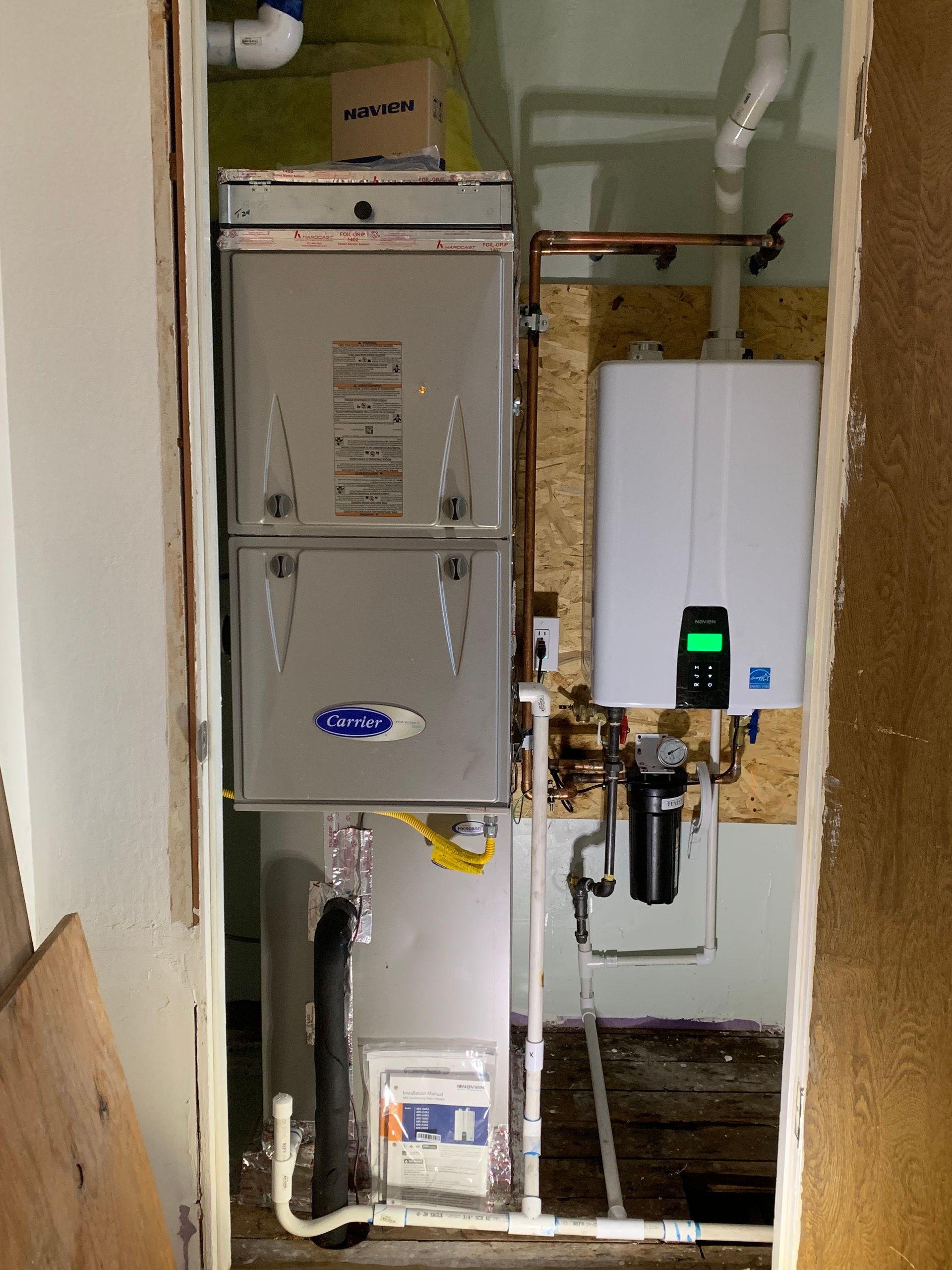 Furnace and water heater in a narrow utility closet. Metal appliances with copper piping and white wall-mounted tankless heater.