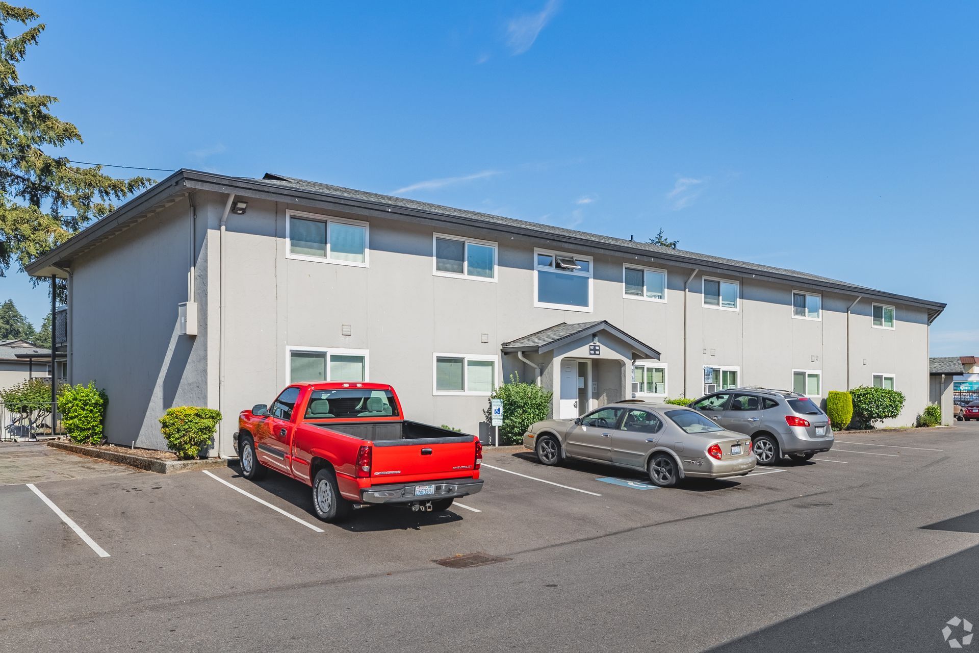 Apartment building with parked red pickup, gray sedan, and SUV under a blue sky