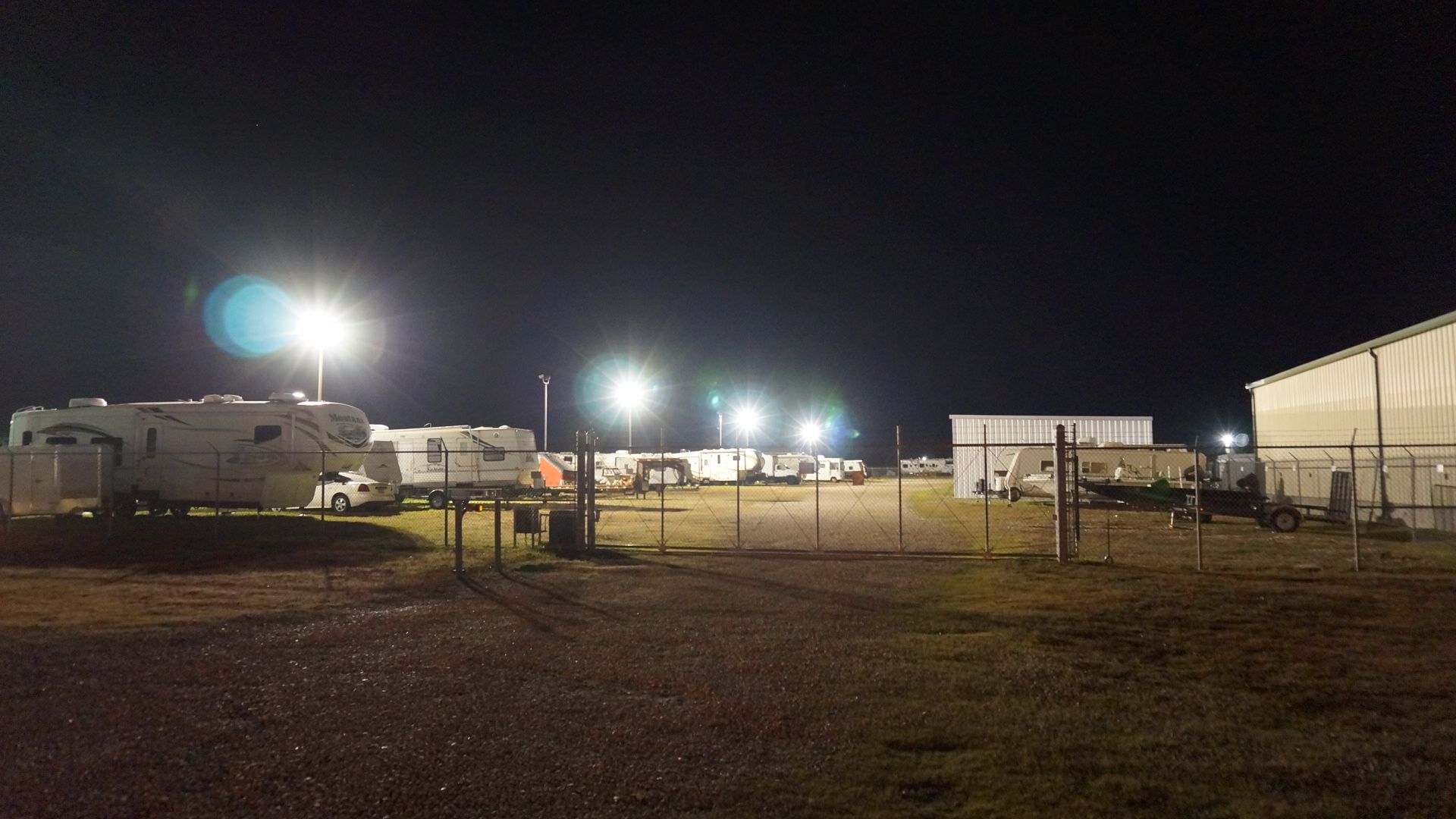 Nighttime scene of trailers and buildings lit by bright spotlights behind a chain-link fence.