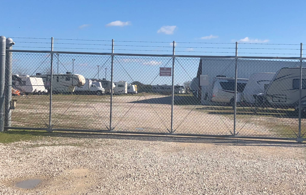 RVs parked in a gravel lot with a long, covered structure under a clear blue sky.