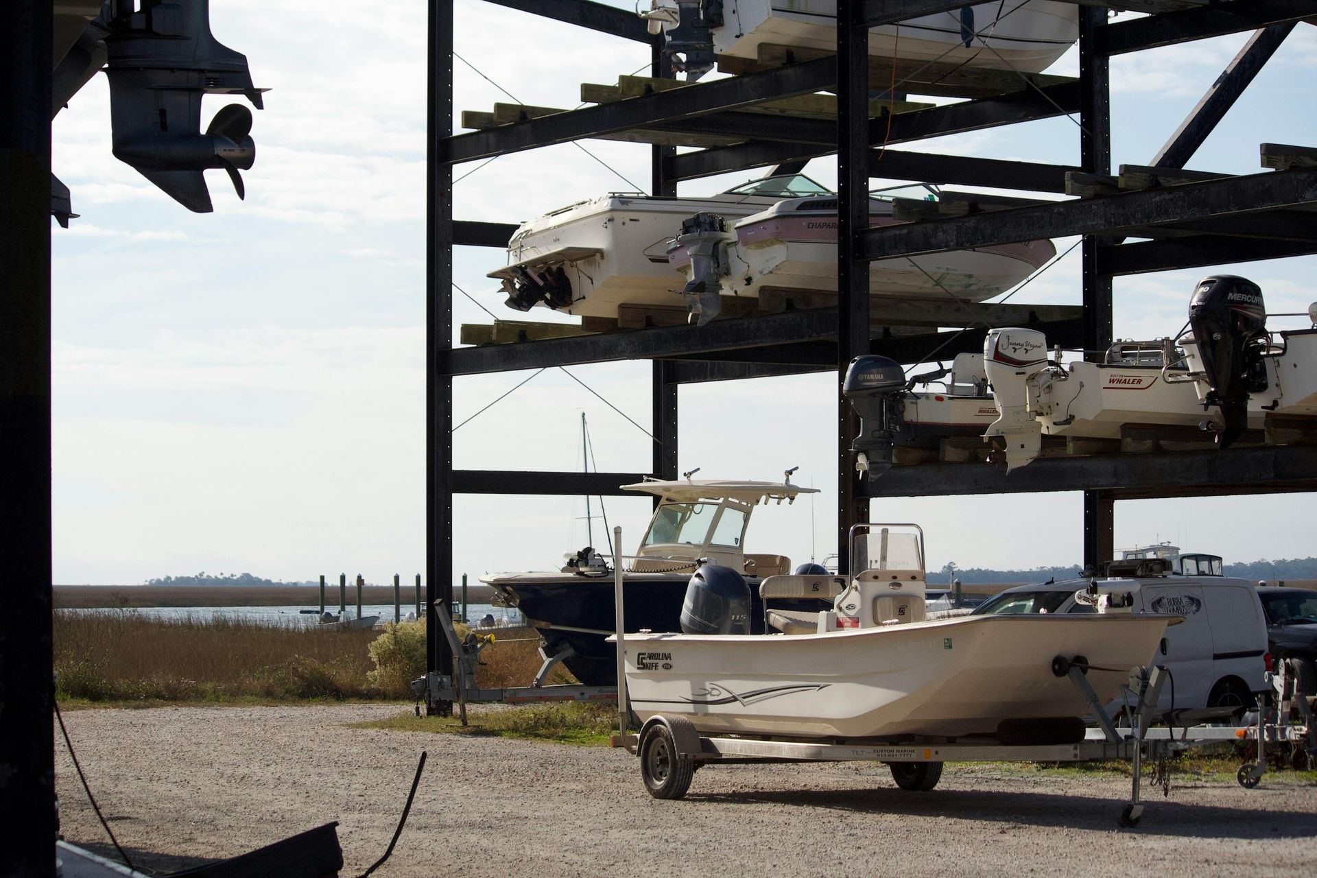Boats stored on multi-level racks at a marina, with one boat on a trailer in front.