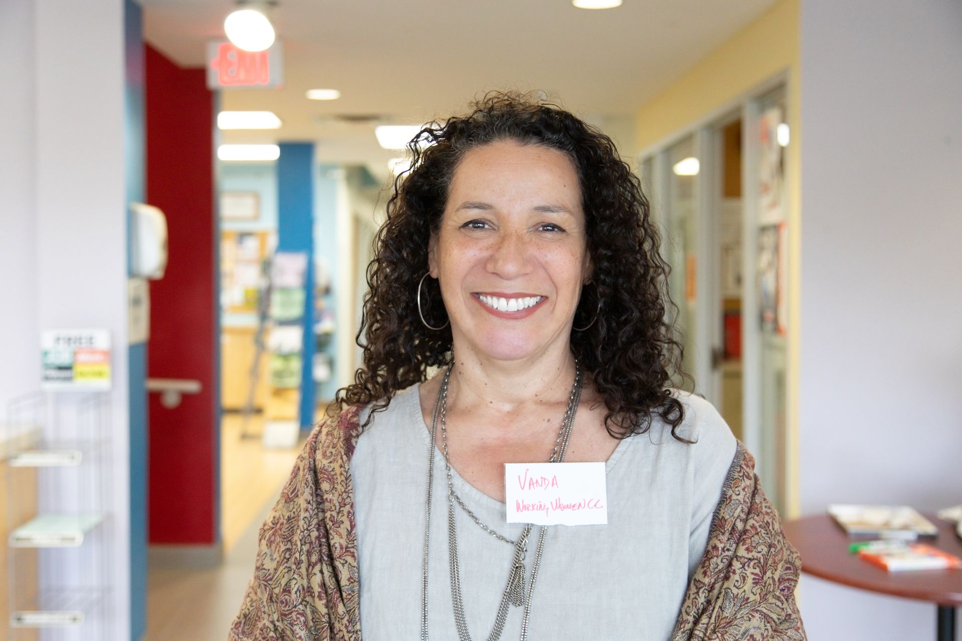 A woman wearing a name tag is smiling in a hallway.