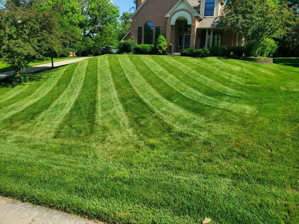 A lush green lawn is being mowed in front of a brick house.