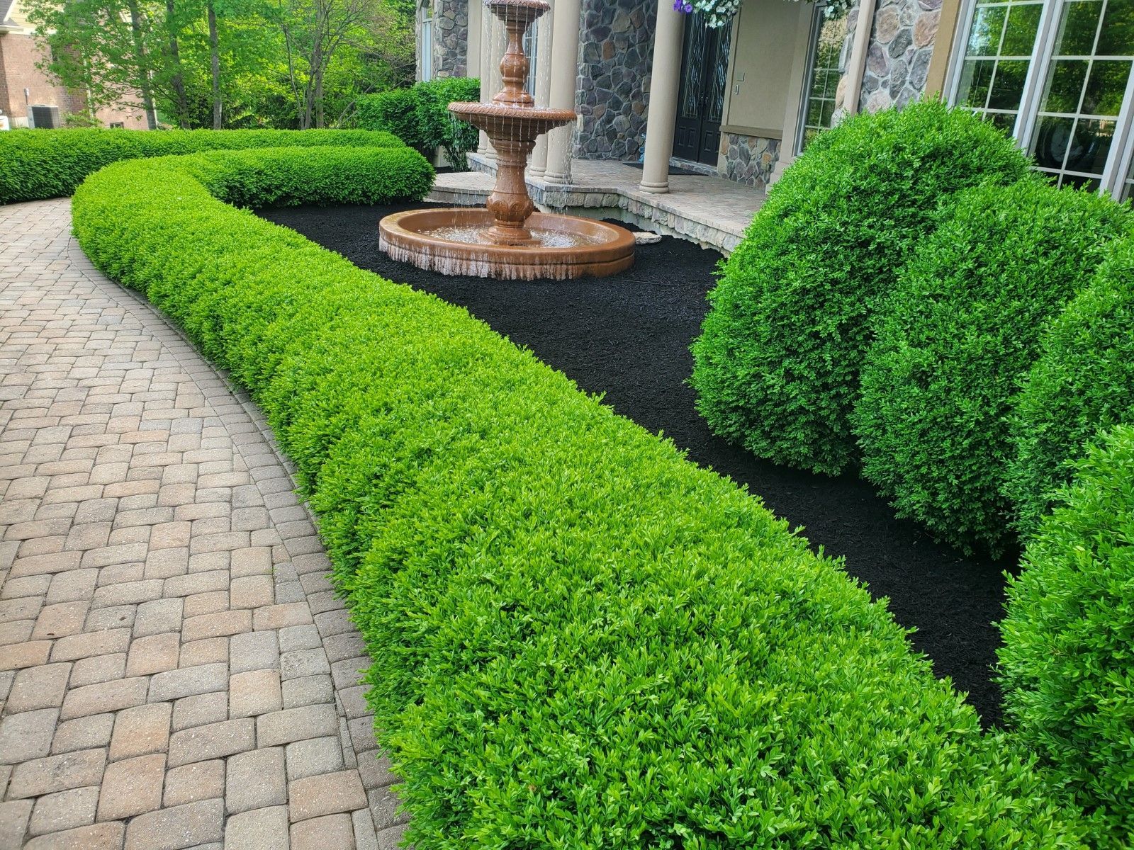 There is a fountain in the middle of the garden surrounded by trimmed bushes.