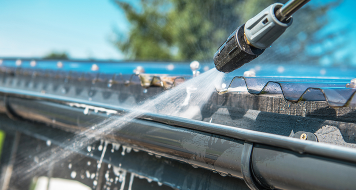 A person is cleaning a gutter with a high pressure washer.