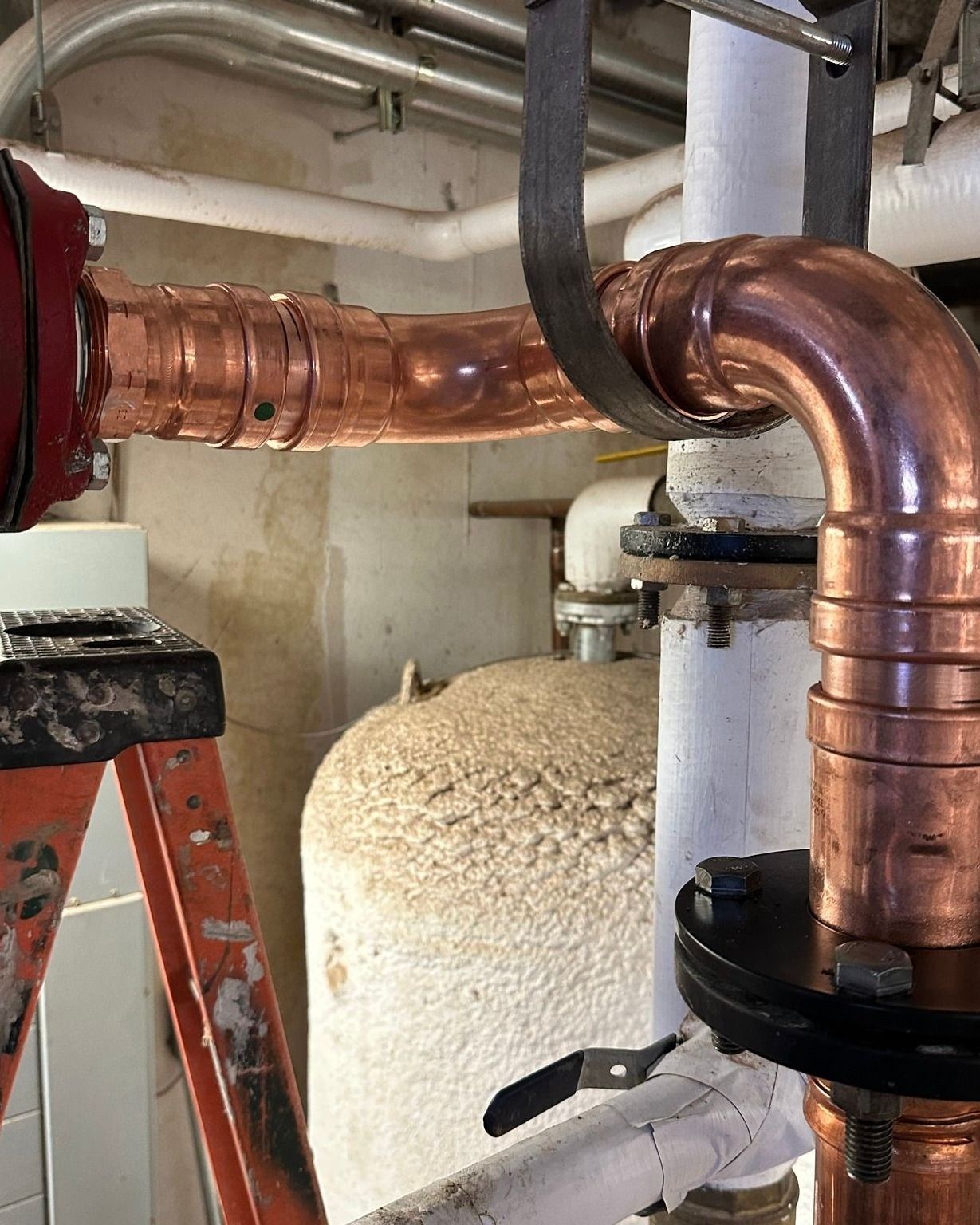 A ladder is sitting next to a copper pipe in a room.