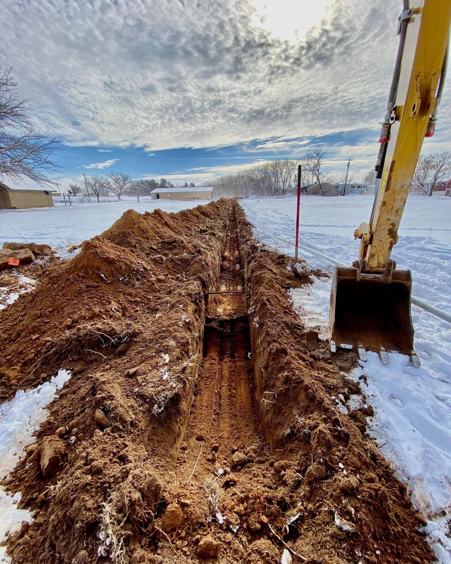 A yellow excavator is digging a trench in the snow.