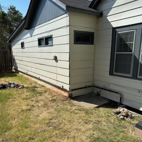 A white house with a gray roof is sitting on top of a lush green field.