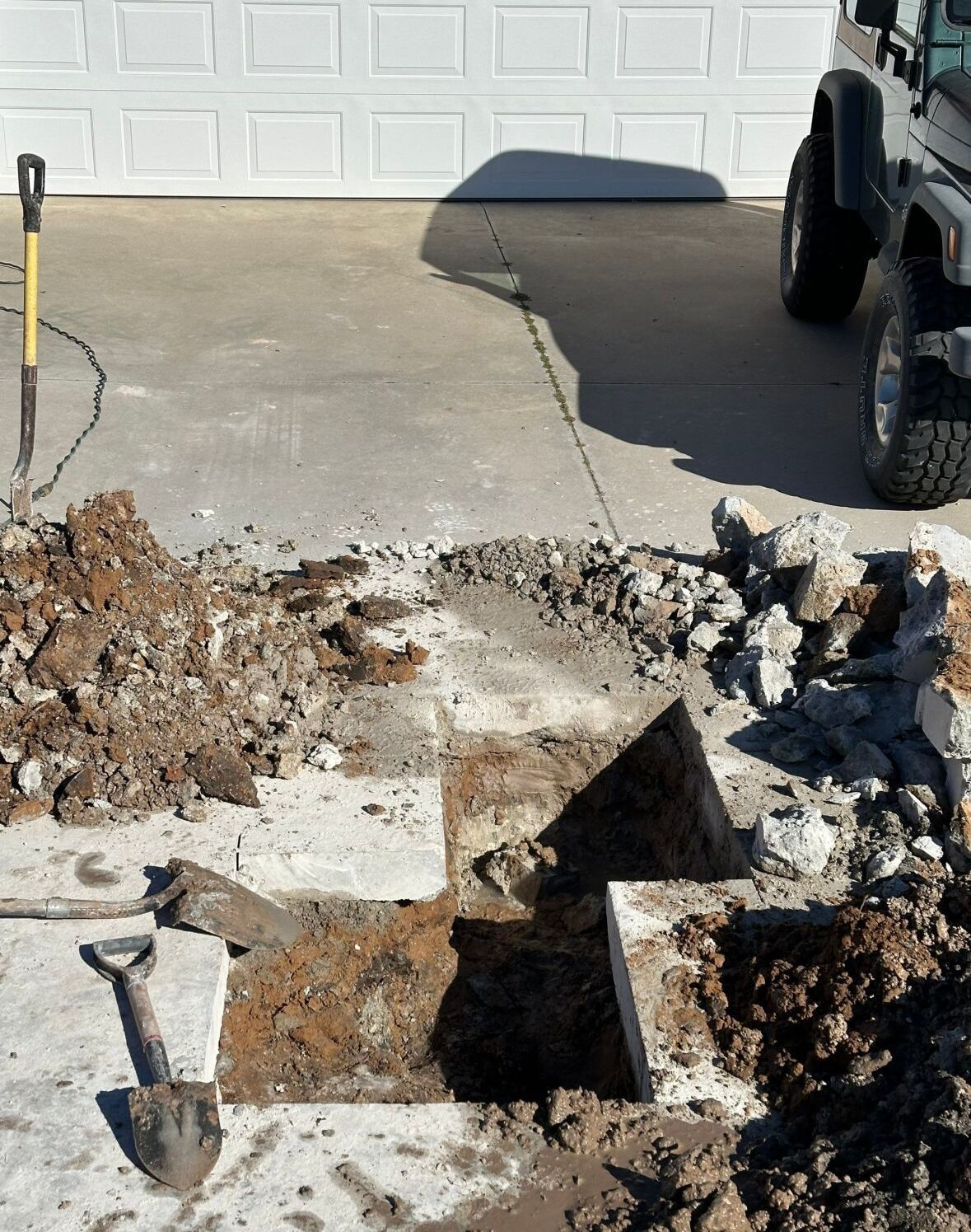 A jeep is parked in a driveway next to a pile of dirt and a shovel