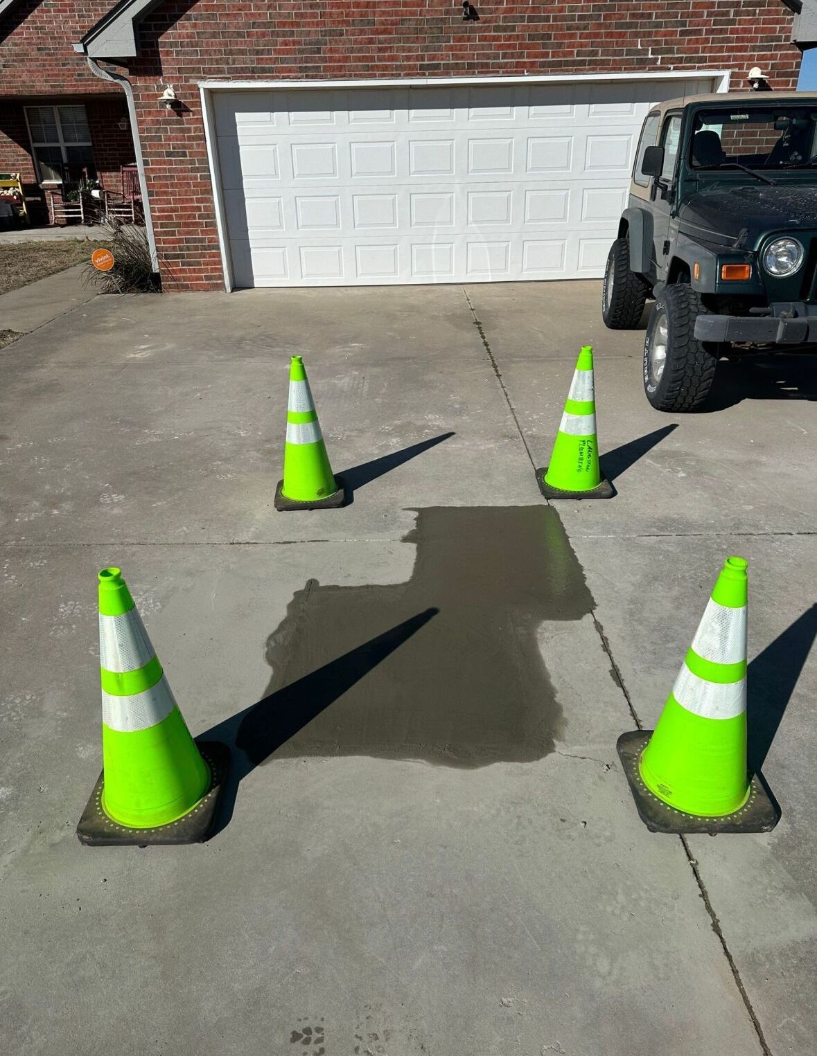 A jeep is parked in a driveway next to three neon green traffic cones.