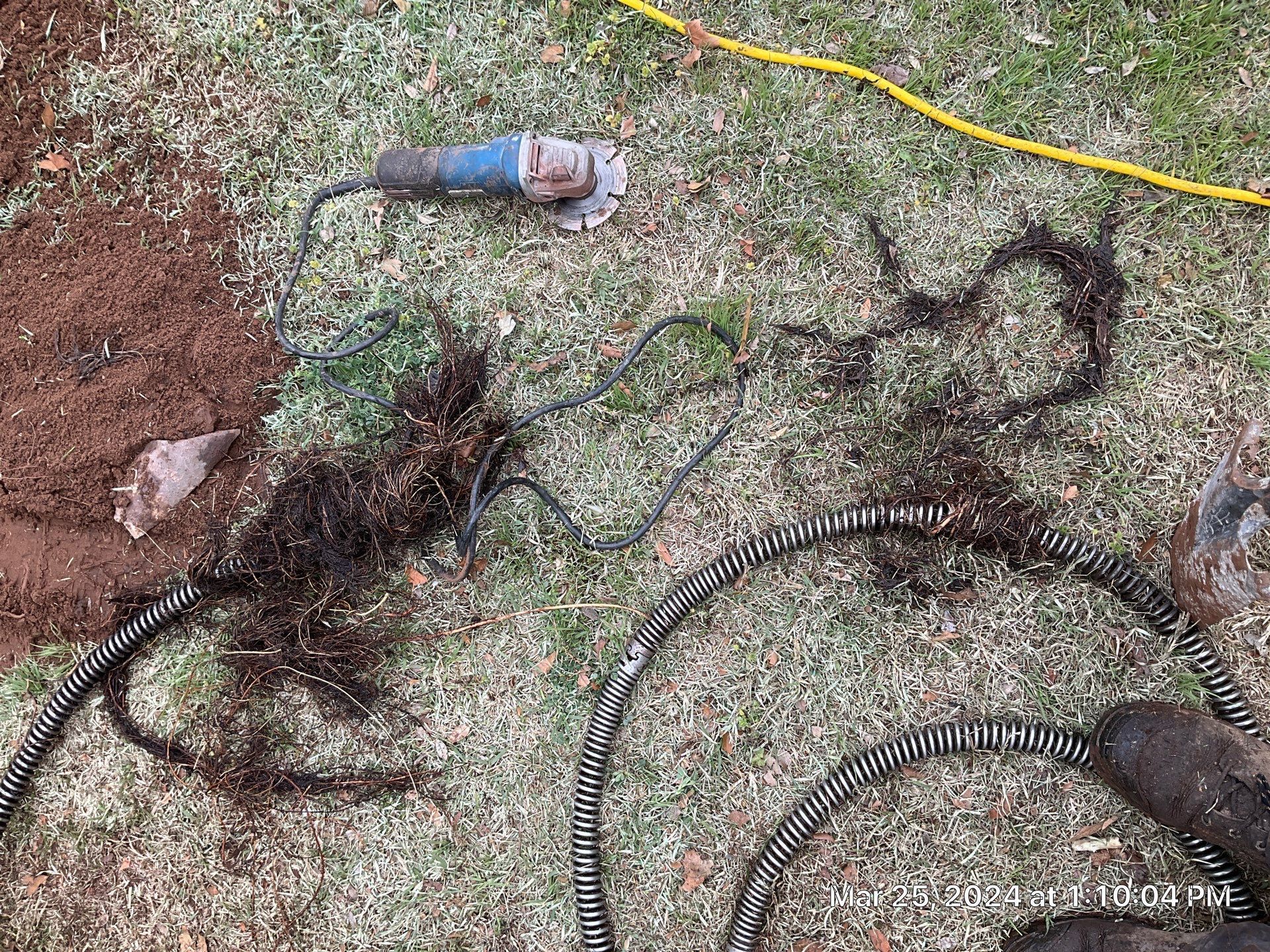 A person is using a grinder to remove roots from a hole in the ground.