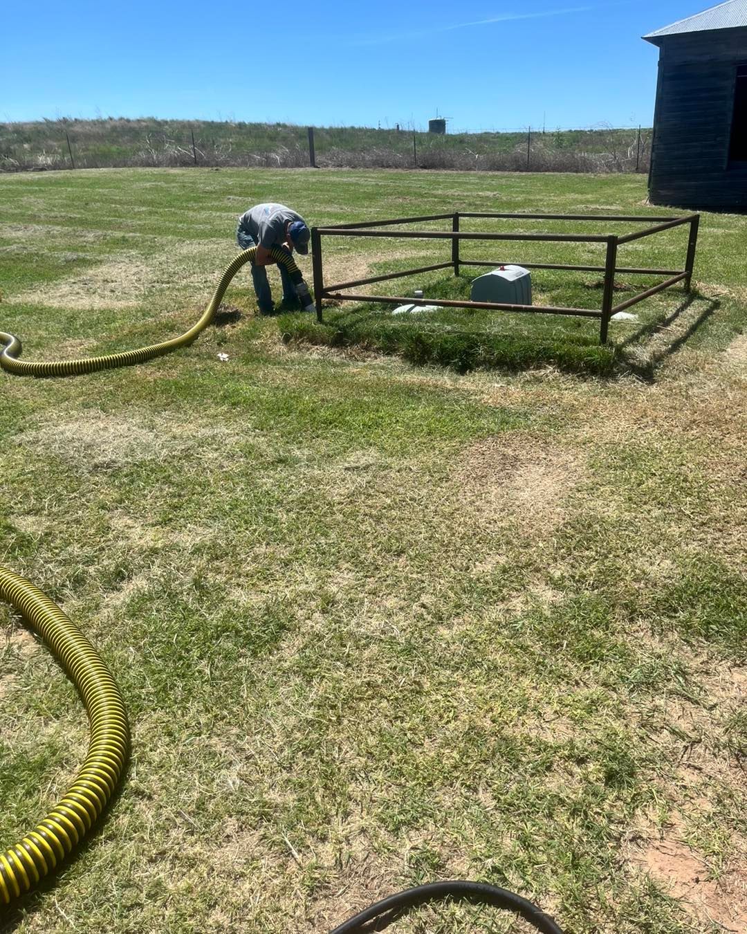 A man is pumping water from a hose in a field.