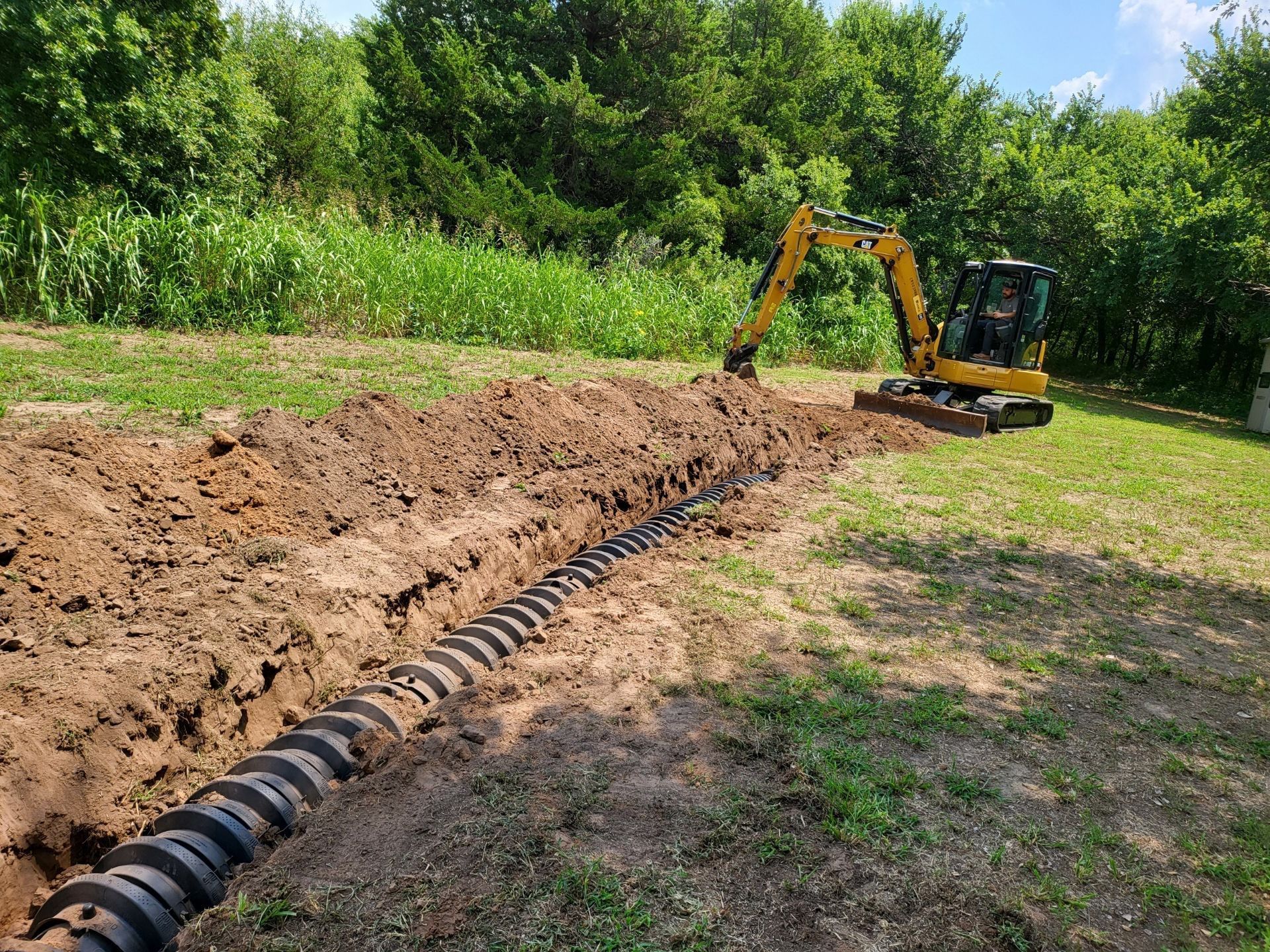 A yellow excavator is digging a trench in a field.