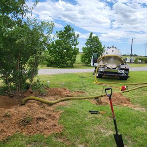 A vacuum truck is sitting in the grass next to a shovel.