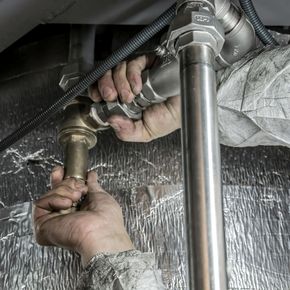 A person is fixing a pipe under a sink with a wrench.