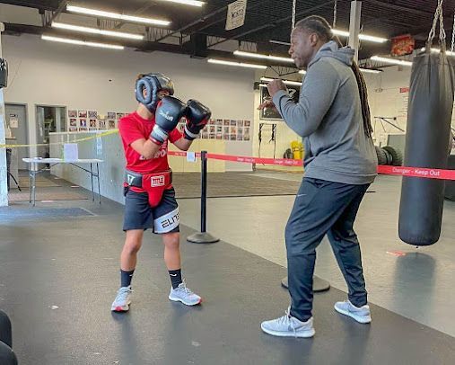 A man is teaching a young boy how to box in a gym.