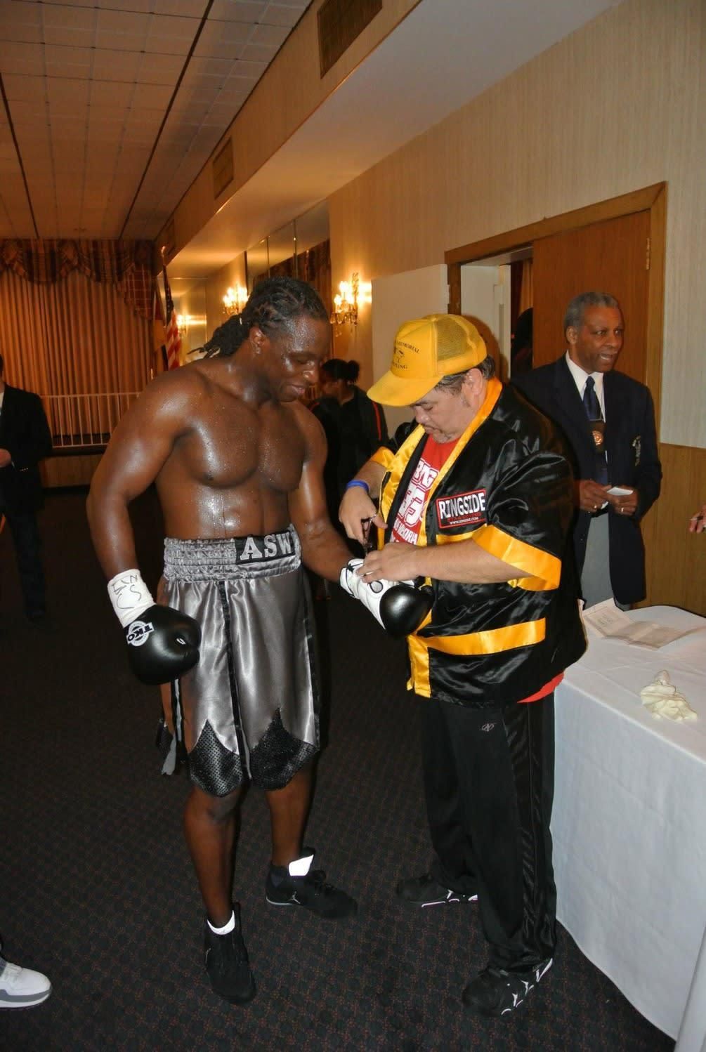 A man in a yellow hat is helping a boxer with his gloves