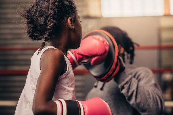 A little girl is boxing with a man in a boxing ring.