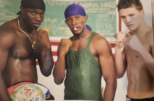 Three men standing next to each other with one wearing a boxing belt