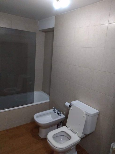 Baño pequeño con bañera, bidé e inodoro bajo paredes de azulejos beige.