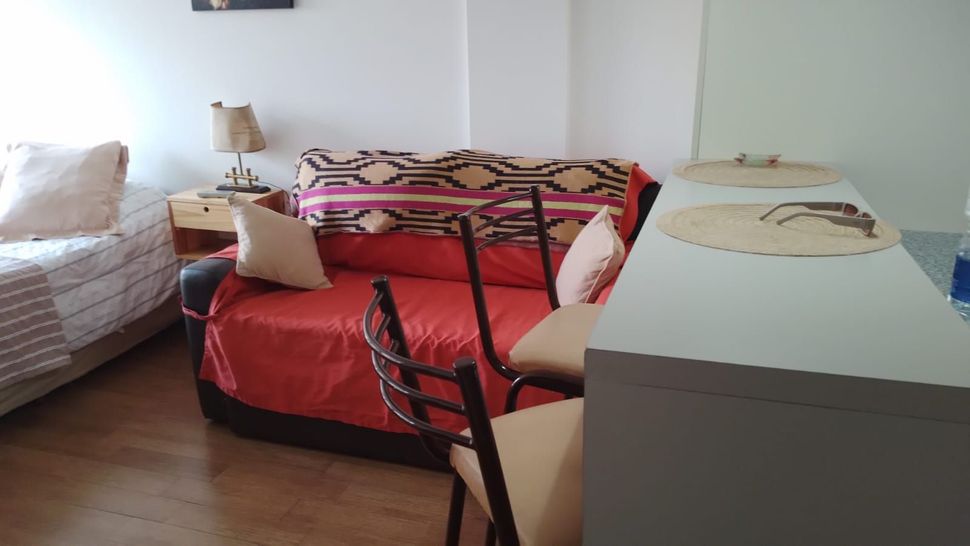 Dormitorio con una colcha roja, cama blanca, cómoda gris y sillas alrededor de la cama.