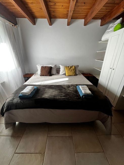Habitación ordenada con cama hecha, armario blanco, vigas de madera a la vista y suelo de baldosas.
