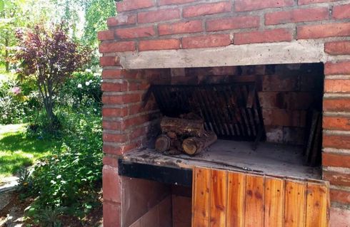 Barbacoa de ladrillo para exteriores con leña en su interior, ubicada en un jardín.
