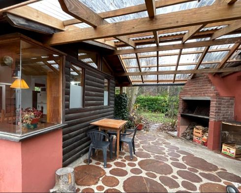Patio cubierto con sendero de piedra, mesa y taburetes de madera y una barbacoa de ladrillo.