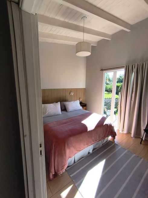 Habitación luminosa con colcha rosa, ropa de cama blanca, cabecero de madera y puertas correderas que dan a un patio soleado.