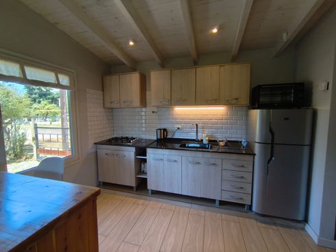 Cocina luminosa con armarios blancos, nevera de acero inoxidable, suelos de madera y luz natural que entra por la ventana.