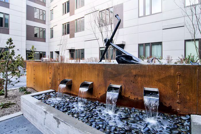 A water fountain in front of a building with a statue of an anchor in the background.
