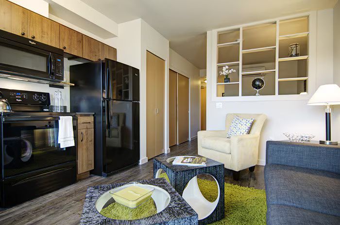 A living room with a couch , chair , coffee table and refrigerator.