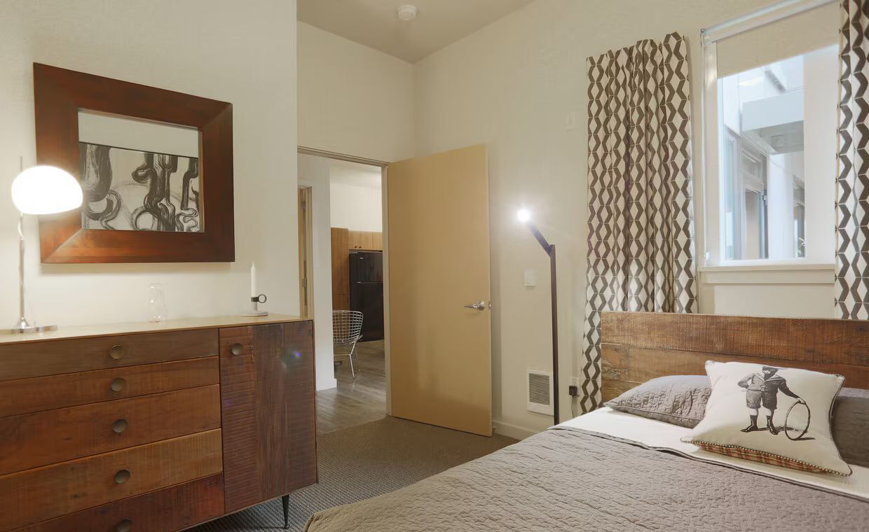 A bedroom with a bed , dresser , lamp and mirror